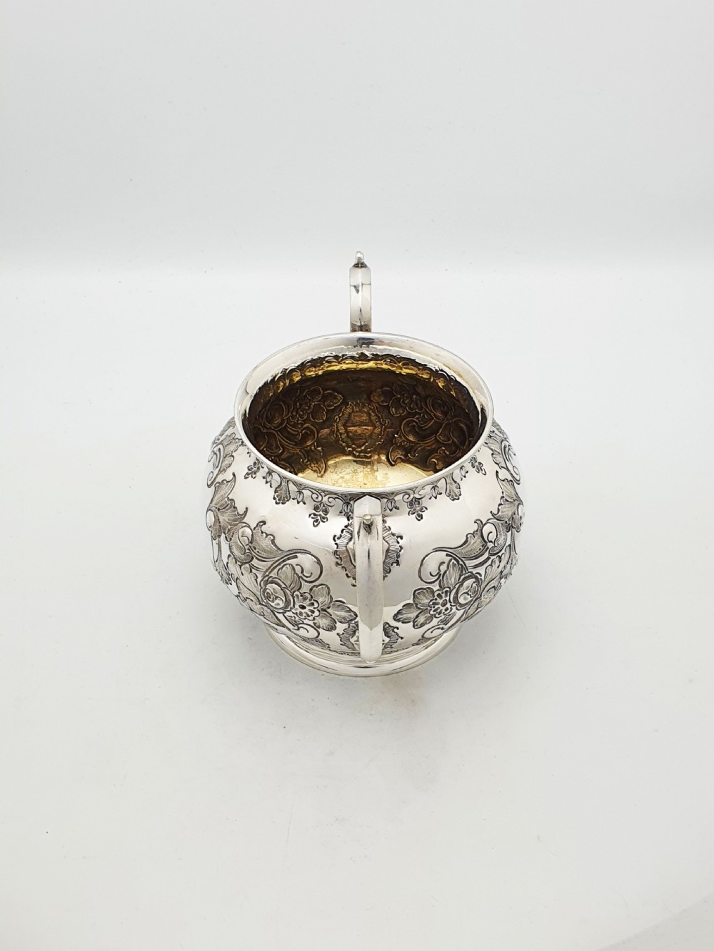 A two-piece Victorian silver-plated set featuring a milk jug and a double-handled sugar bowl, both decorated with intricate repousse floral scrollwork and lined with a gilded interior. View V
