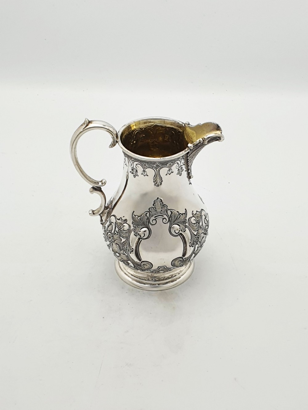A two-piece Victorian silver-plated set featuring a milk jug and a double-handled sugar bowl, both decorated with intricate repousse floral scrollwork and lined with a gilded interior. View X