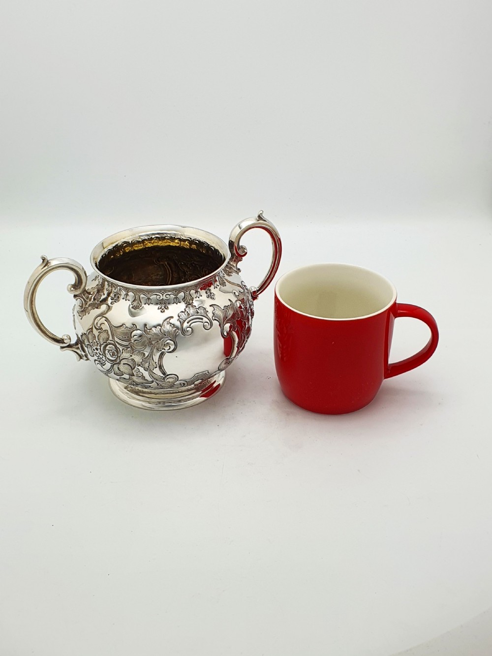 A two-piece Victorian silver-plated set featuring a milk jug and a double-handled sugar bowl, both decorated with intricate repousse floral scrollwork and lined with a gilded interior. View XV