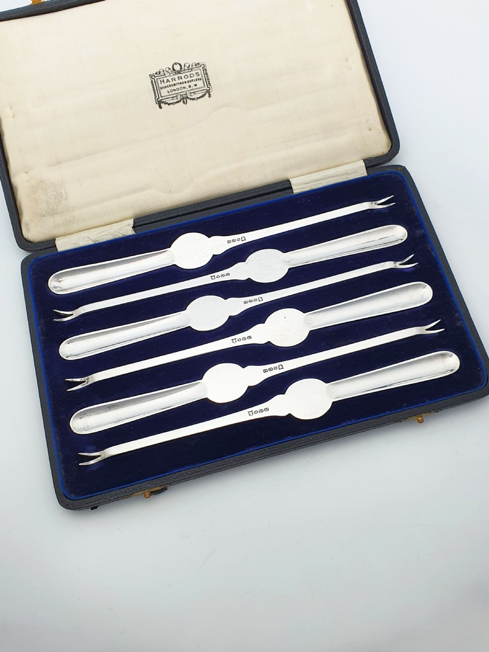 A cased set of six silver-plated lobster picks displayed inside a dark blue velvet-lined presentation box.