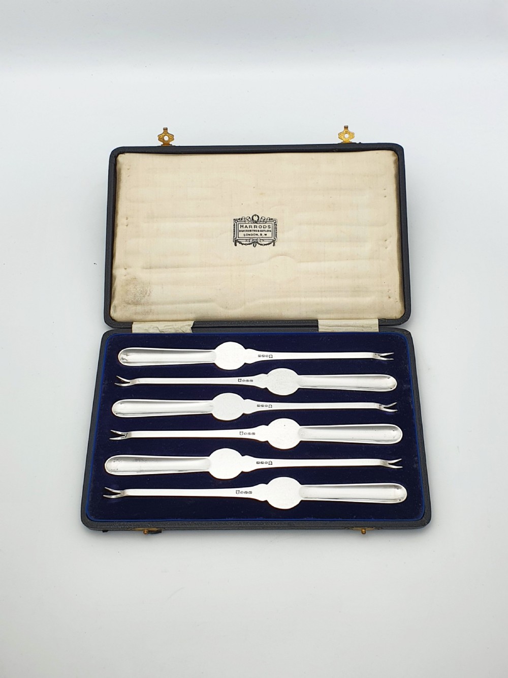 A cased set of six silver-plated lobster picks displayed inside a dark blue velvet-lined presentation box. View III