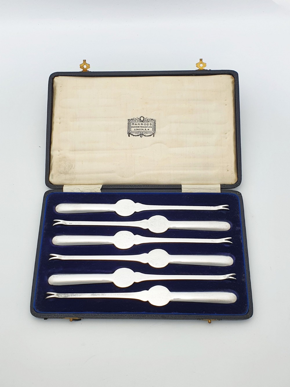 A cased set of six silver-plated lobster picks displayed inside a dark blue velvet-lined presentation box. View VI