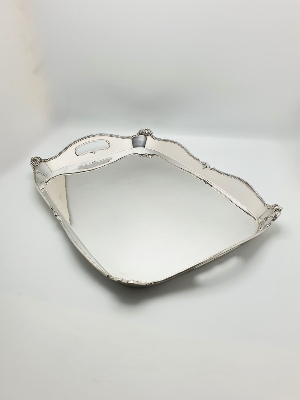 An Edwardian rectangular silver-plated serving tray featuring raised sides, integral hand-holds, and decorative shell and scroll details along the rim.