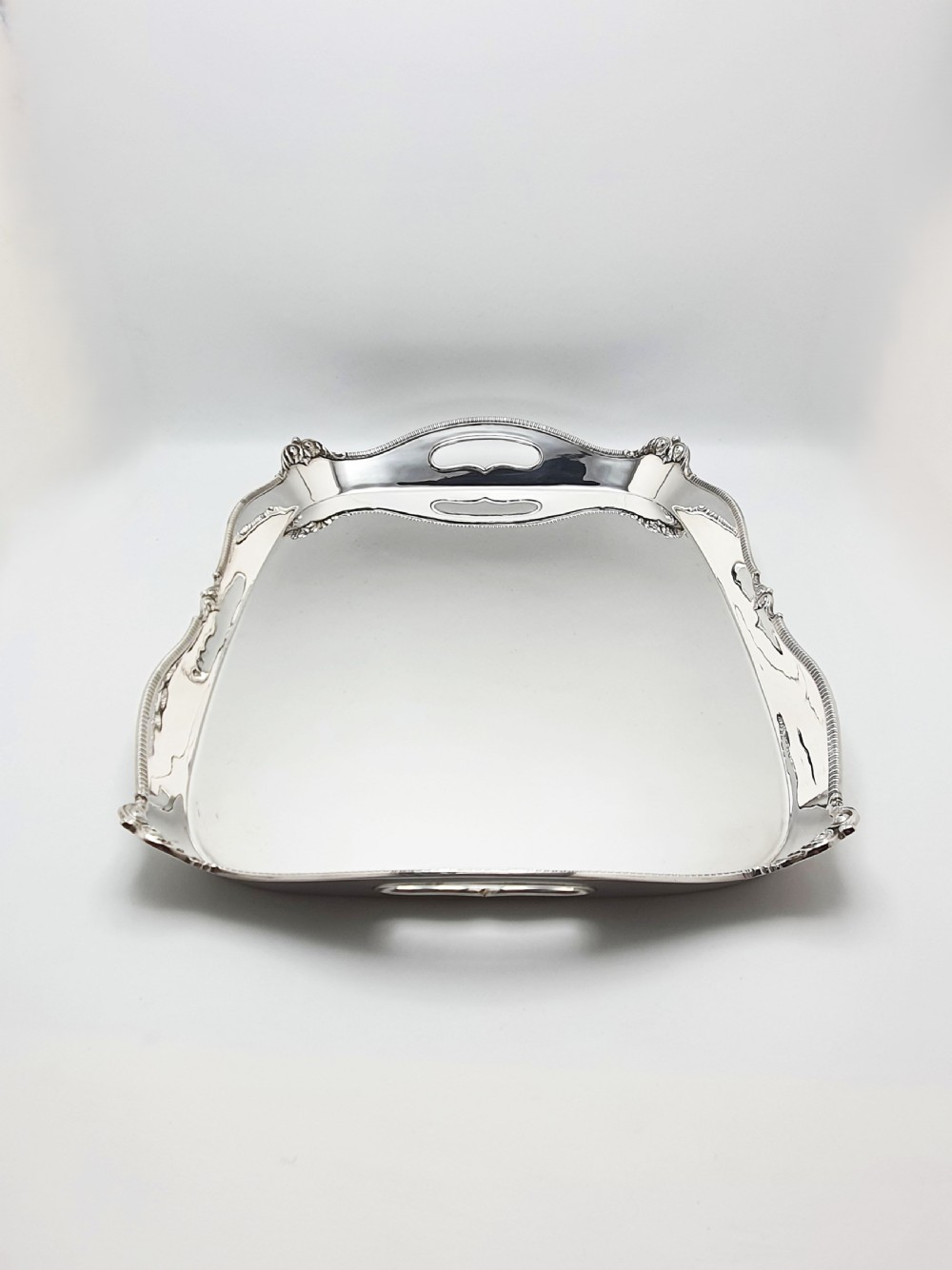 An Edwardian rectangular silver-plated serving tray featuring raised sides, integral hand-holds, and decorative shell and scroll details along the rim. View V