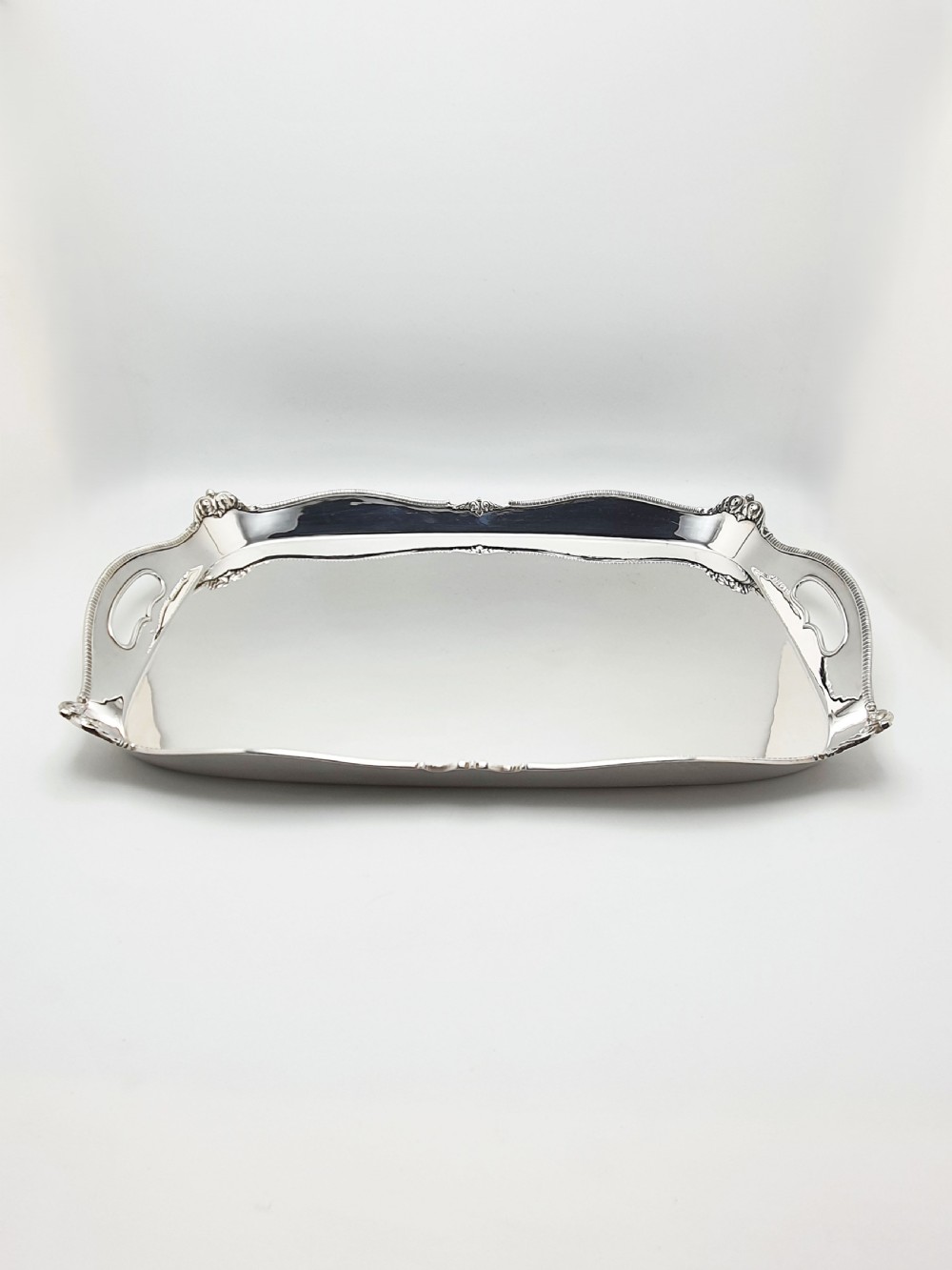 An Edwardian rectangular silver-plated serving tray featuring raised sides, integral hand-holds, and decorative shell and scroll details along the rim. View VI