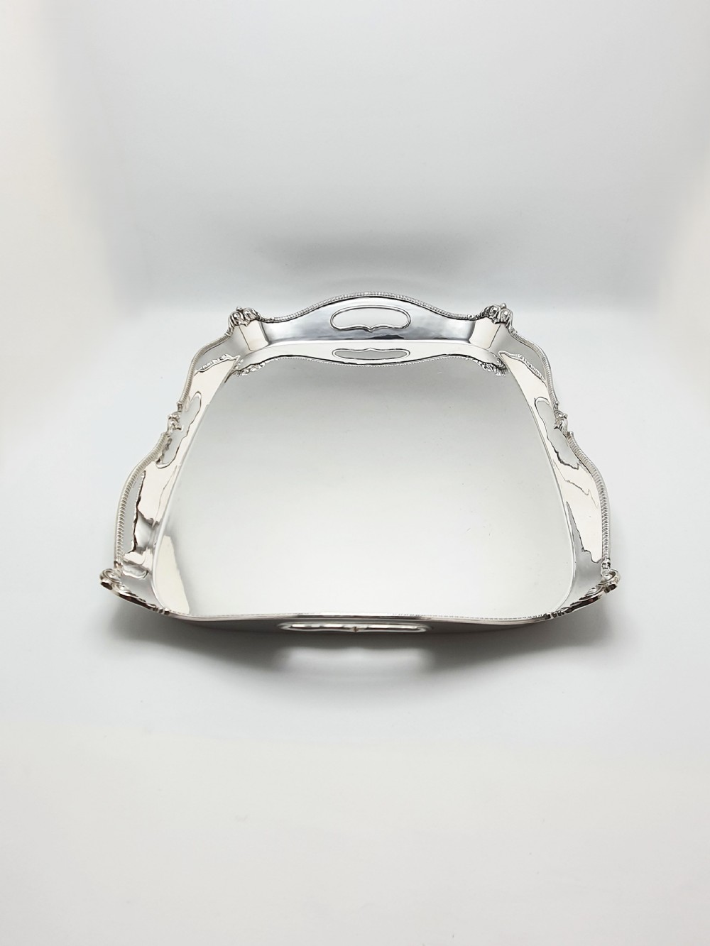 An Edwardian rectangular silver-plated serving tray featuring raised sides, integral hand-holds, and decorative shell and scroll details along the rim. View VII