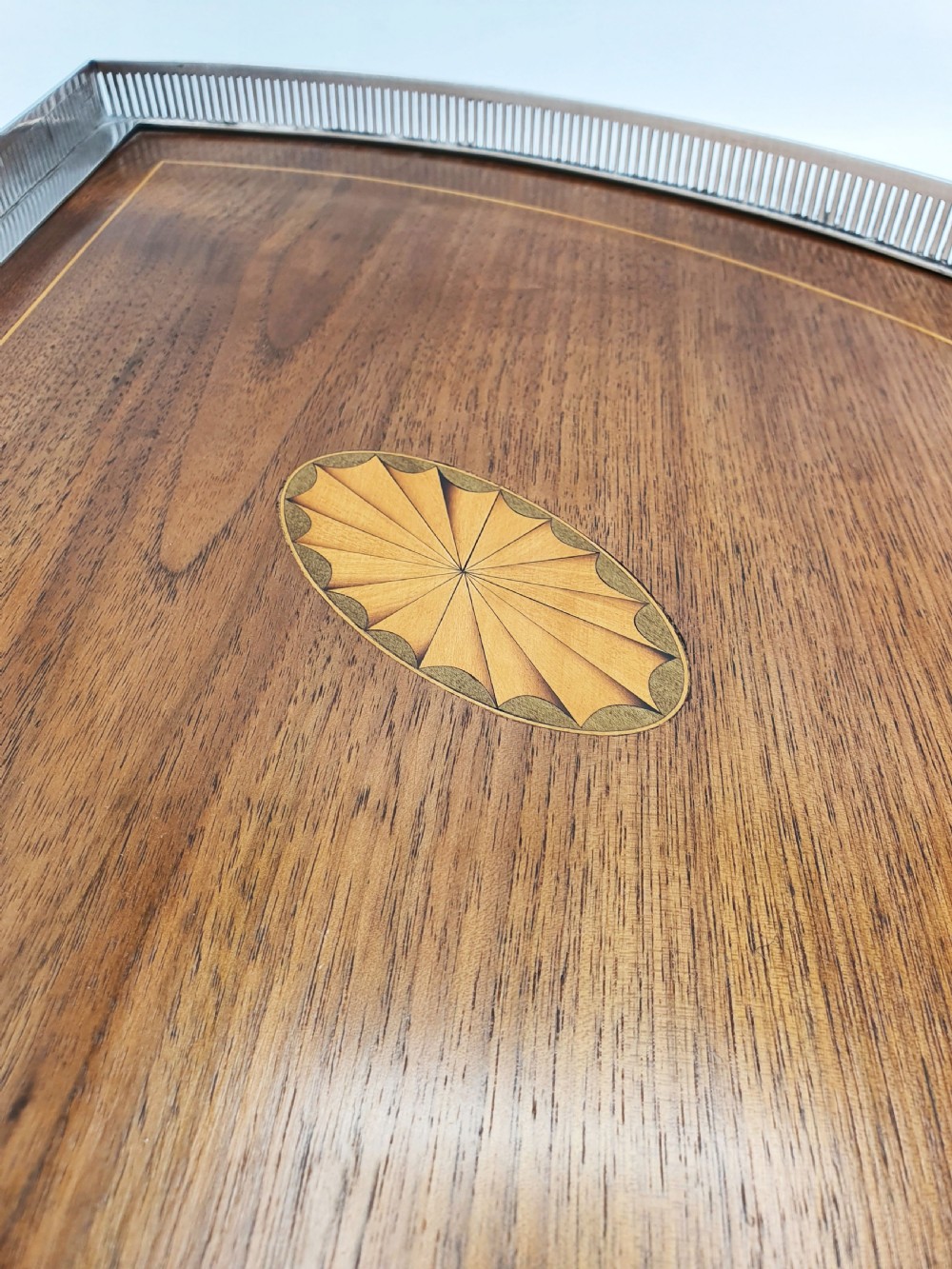 A fan-shaped Edwardian mahogany serving tray featuring an inlaid oval patera motif, fine line stringing, and a pierced silver-plated gallery rim with handles and ball feet. View II