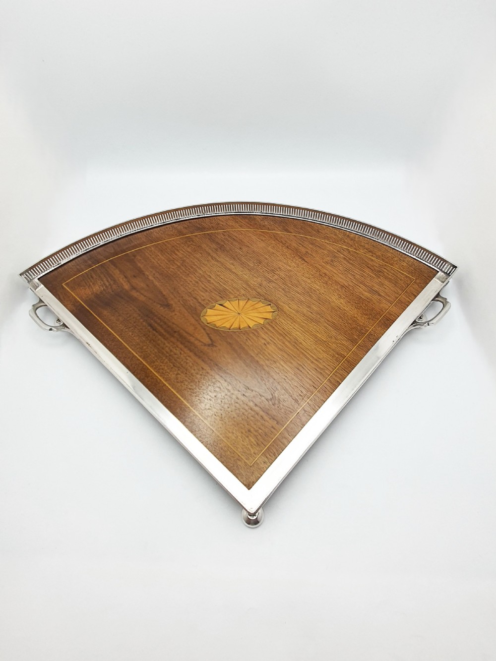 A fan-shaped Edwardian mahogany serving tray featuring an inlaid oval patera motif, fine line stringing, and a pierced silver-plated gallery rim with handles and ball feet. View IV