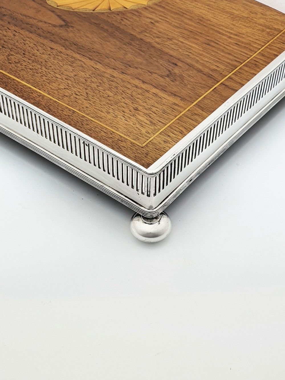 A fan-shaped Edwardian mahogany serving tray featuring an inlaid oval patera motif, fine line stringing, and a pierced silver-plated gallery rim with handles and ball feet. View V