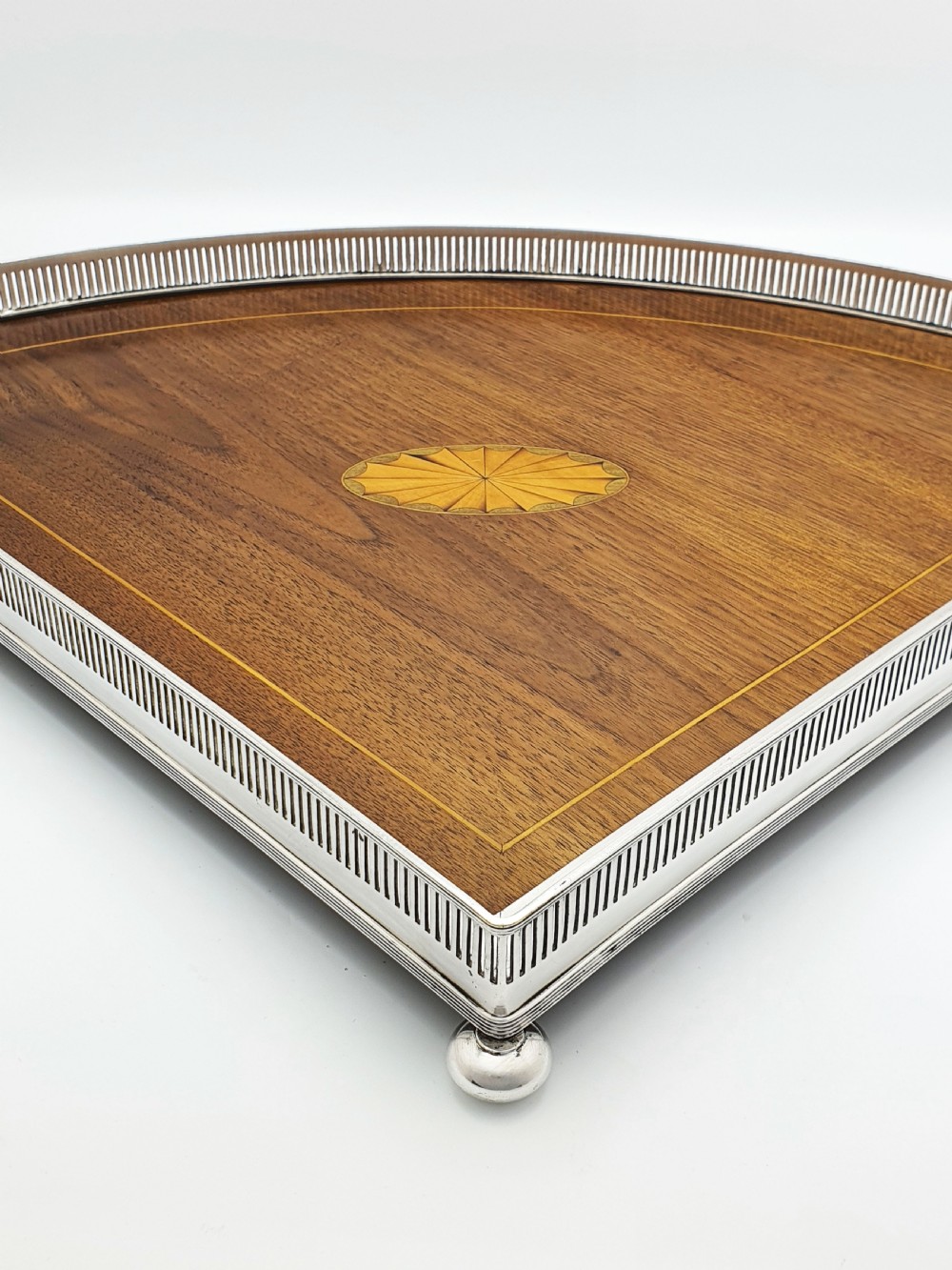 A fan-shaped Edwardian mahogany serving tray featuring an inlaid oval patera motif, fine line stringing, and a pierced silver-plated gallery rim with handles and ball feet. View VI