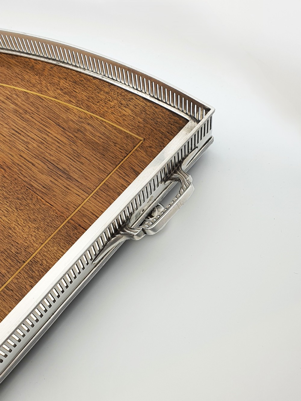 A fan-shaped Edwardian mahogany serving tray featuring an inlaid oval patera motif, fine line stringing, and a pierced silver-plated gallery rim with handles and ball feet. View VII