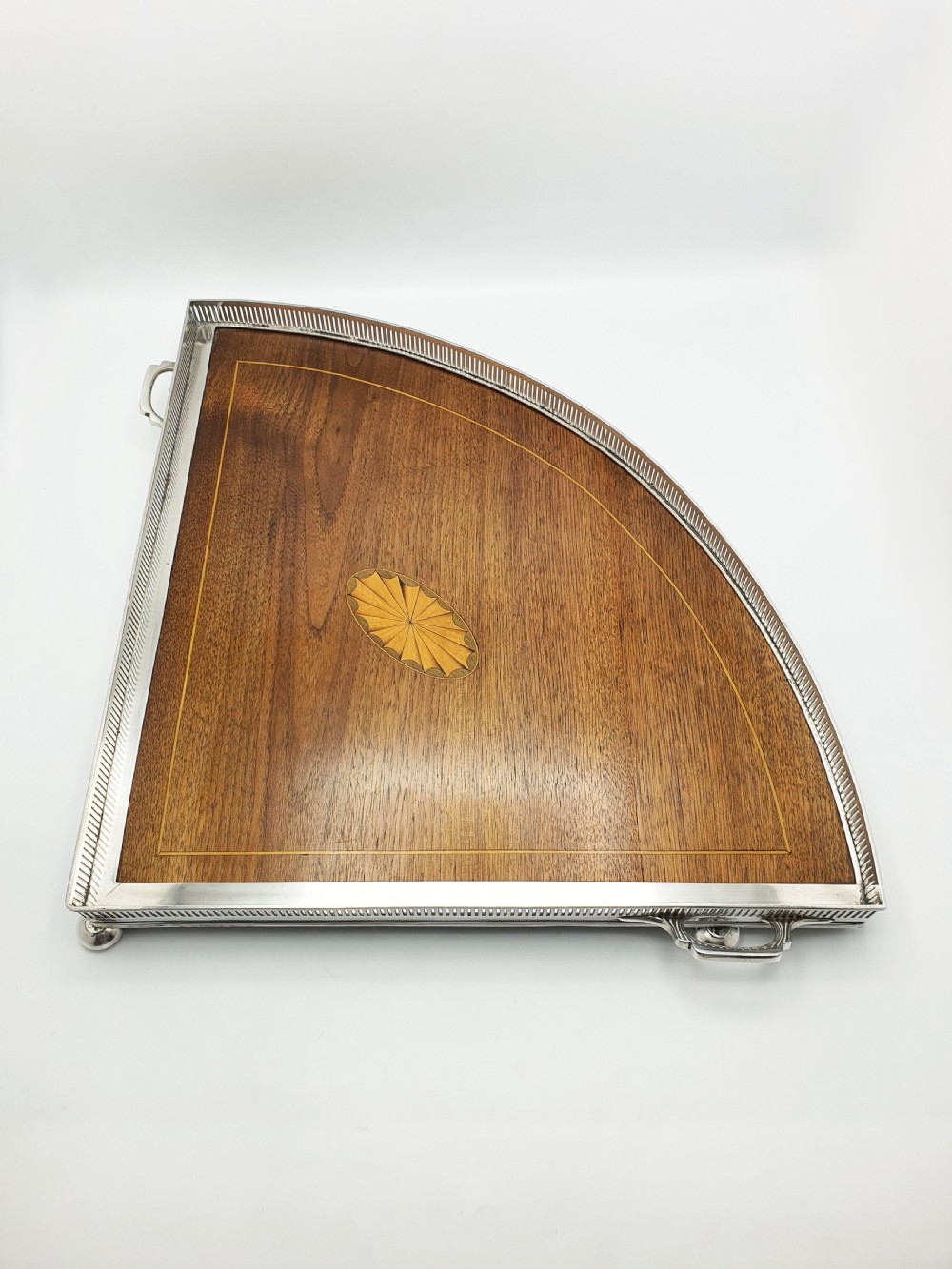A fan-shaped Edwardian mahogany serving tray featuring an inlaid oval patera motif, fine line stringing, and a pierced silver-plated gallery rim with handles and ball feet. View VIII