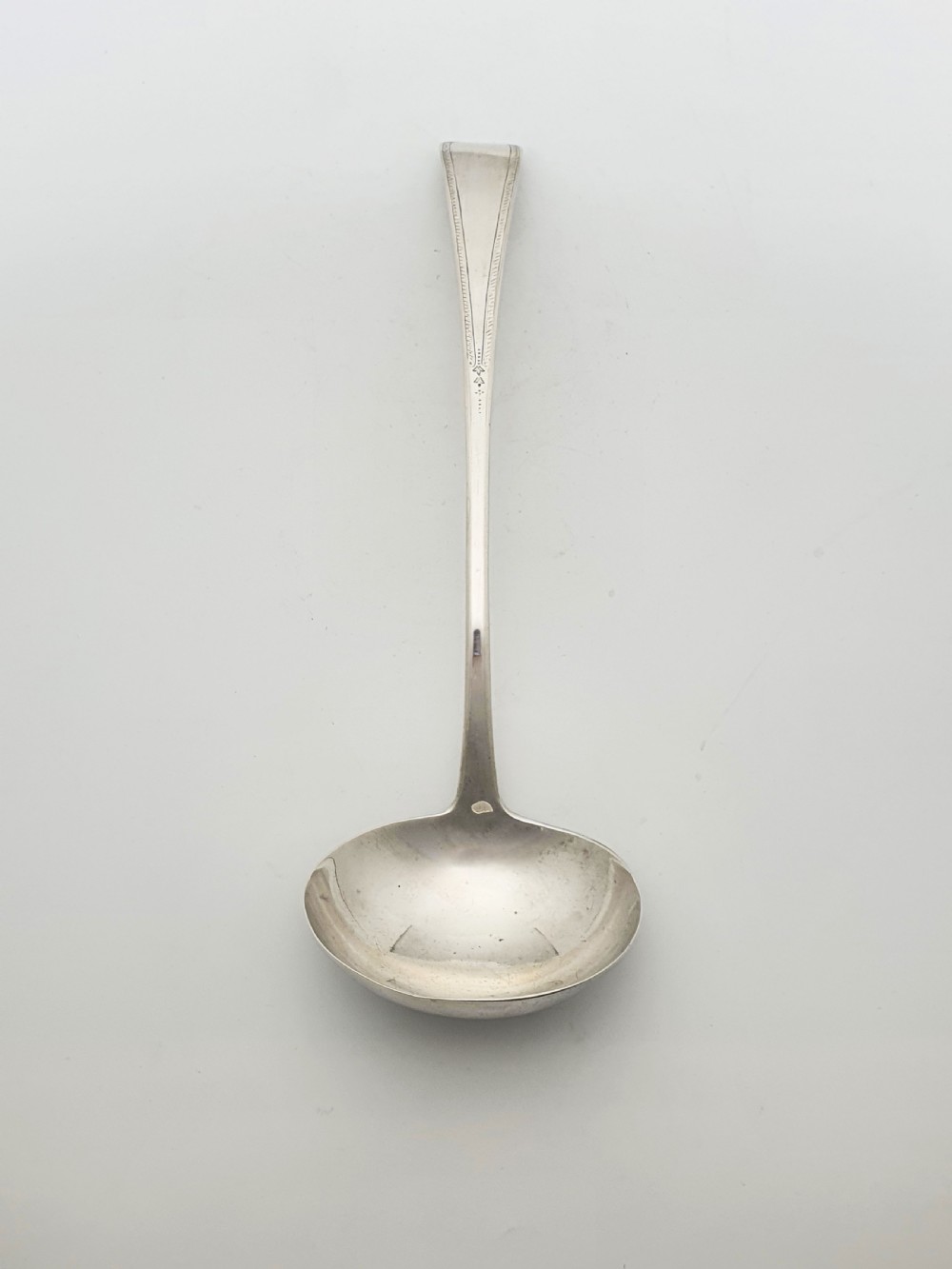 A Georgian sterling silver soup ladle dated 1824 featuring a long tapered handle with a subtle threaded border and a deep oval bowl.