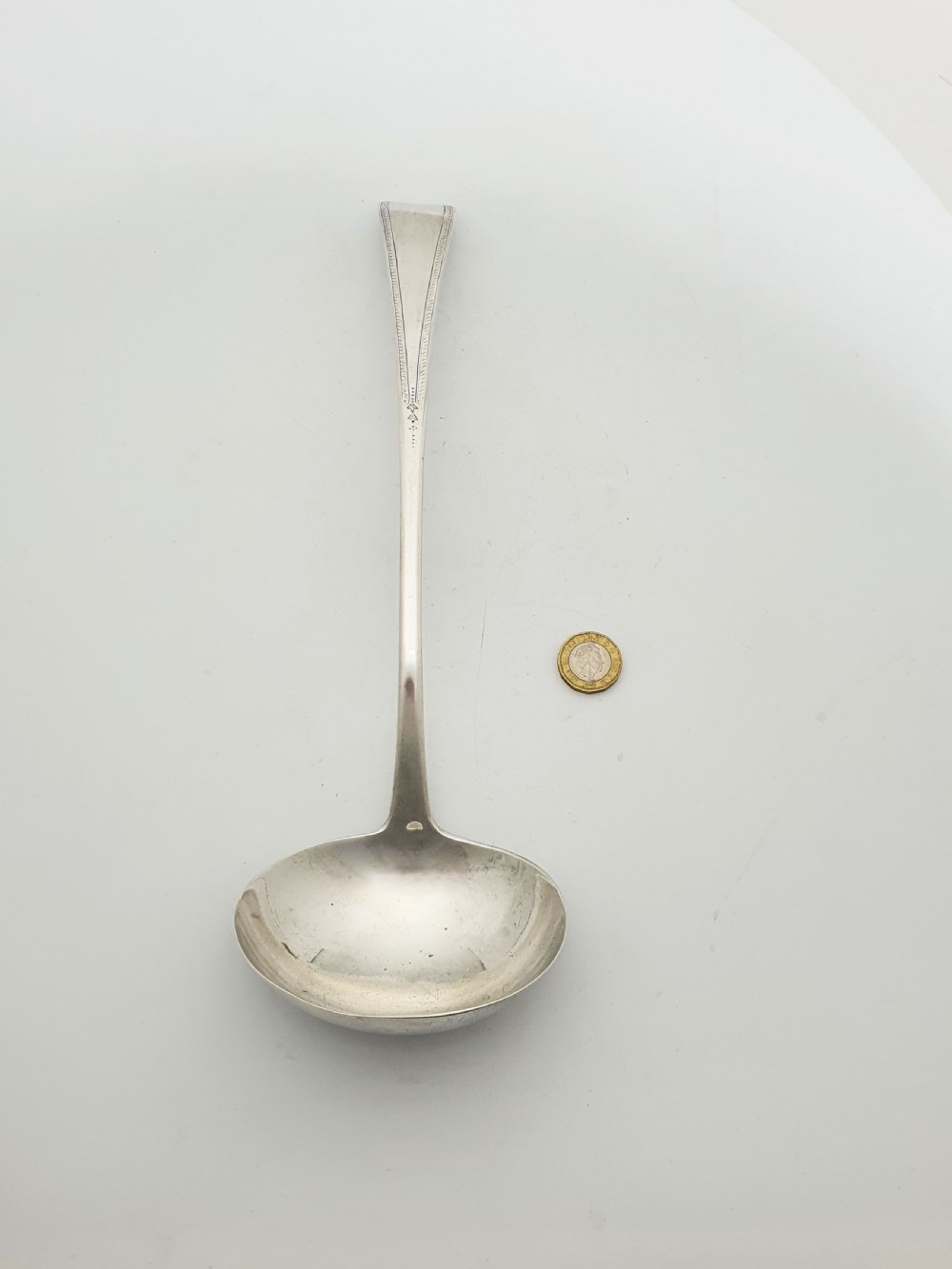 A Georgian sterling silver soup ladle dated 1824 featuring a long tapered handle with a subtle threaded border and a deep oval bowl. View V