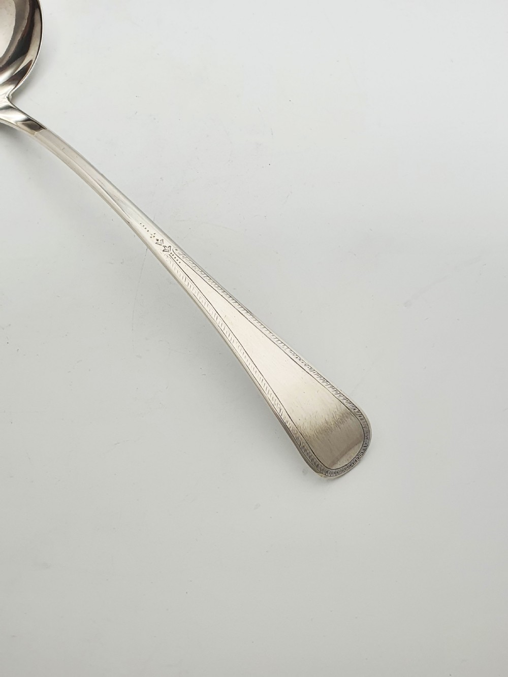 A Georgian sterling silver soup ladle dated 1824 featuring a long tapered handle with a subtle threaded border and a deep oval bowl. View VI
