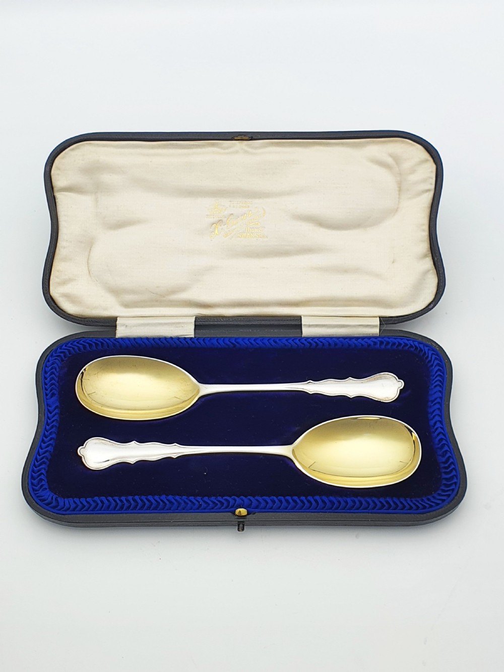 A pair of 1910 sterling silver serving spoons with gilt oval bowls presented inside a dark blue velvet-lined case.