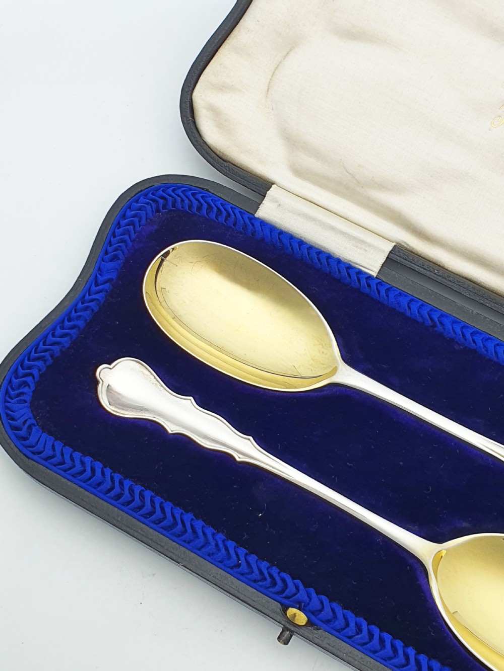 A pair of 1910 sterling silver serving spoons with gilt oval bowls presented inside a dark blue velvet-lined case. View III