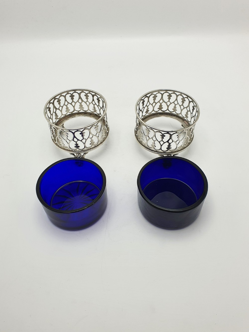 A pair of circular pierced sterling silver salt cellars containing dark cobalt blue glass liners with accompanying engraved silver spoons. View VII