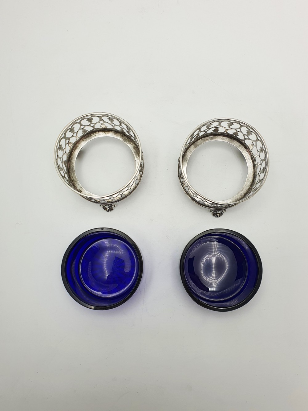A pair of circular pierced sterling silver salt cellars containing dark cobalt blue glass liners with accompanying engraved silver spoons. View VIII
