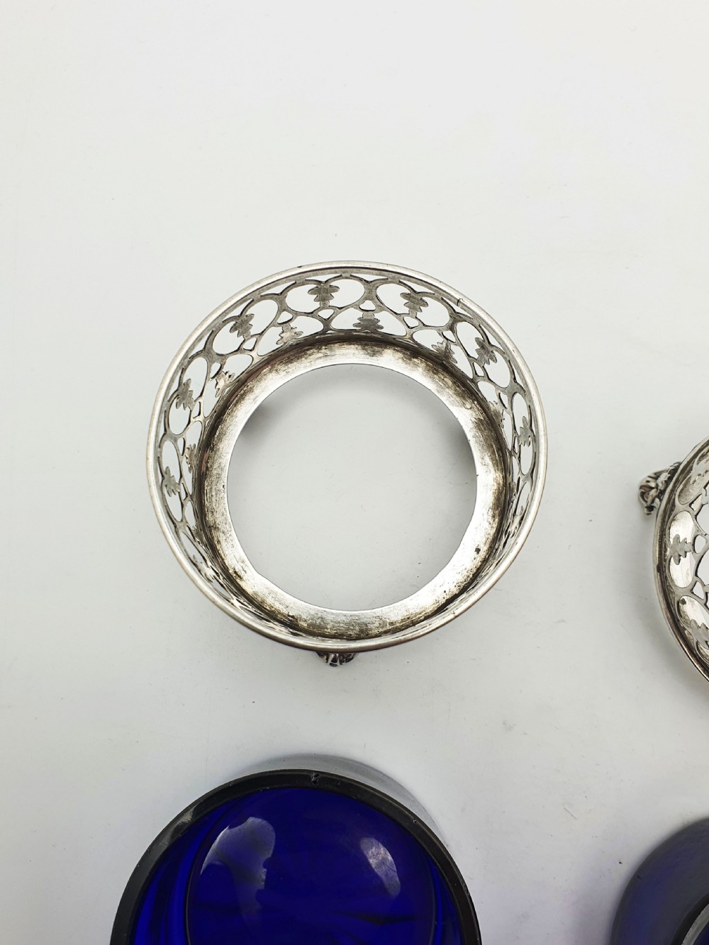 A pair of circular pierced sterling silver salt cellars containing dark cobalt blue glass liners with accompanying engraved silver spoons. View X