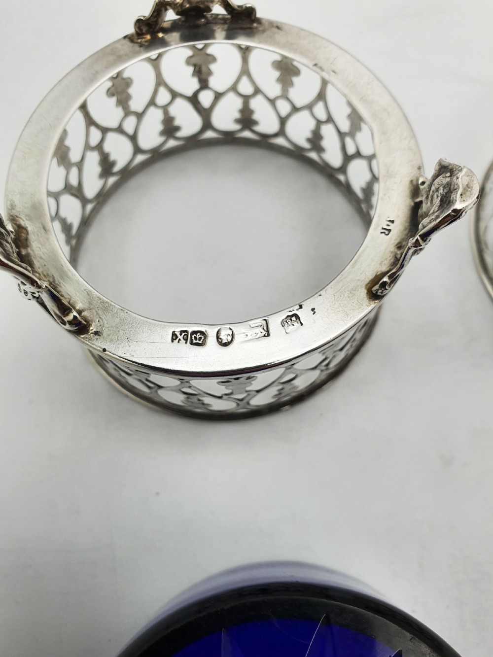 A pair of circular pierced sterling silver salt cellars containing dark cobalt blue glass liners with accompanying engraved silver spoons. View XII