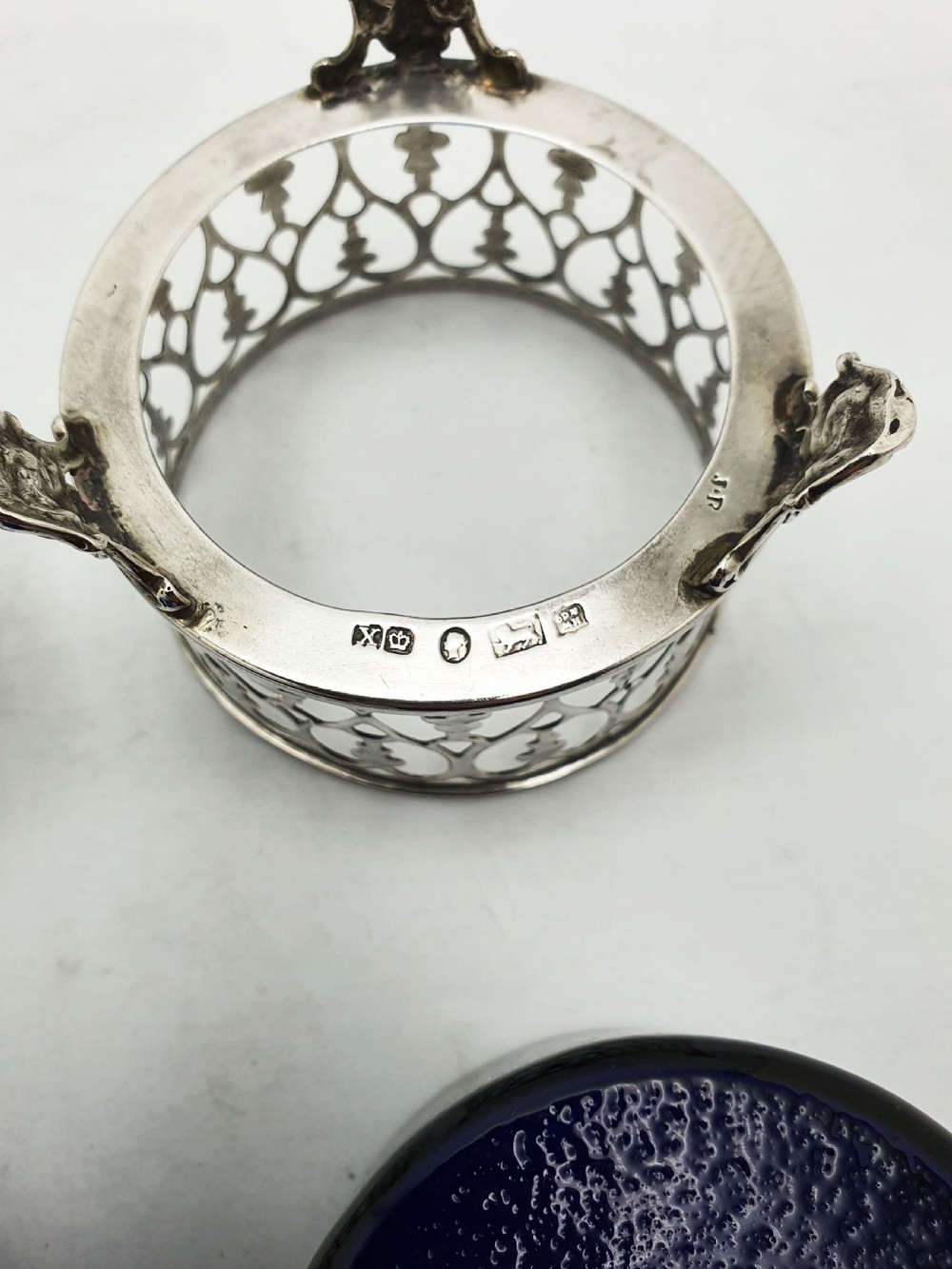 A pair of circular pierced sterling silver salt cellars containing dark cobalt blue glass liners with accompanying engraved silver spoons. View XIII