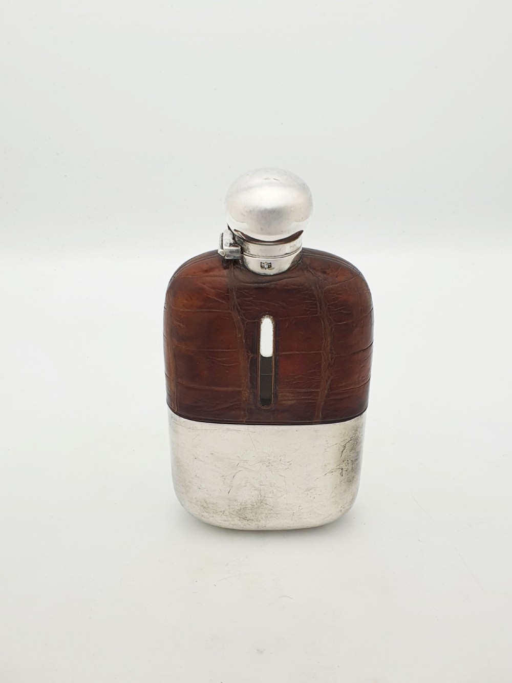 An antique Edwardian hip flask featuring a brown crocodile skin upper section with a vertical sight slot and a silver-plated lower removable cup. View II