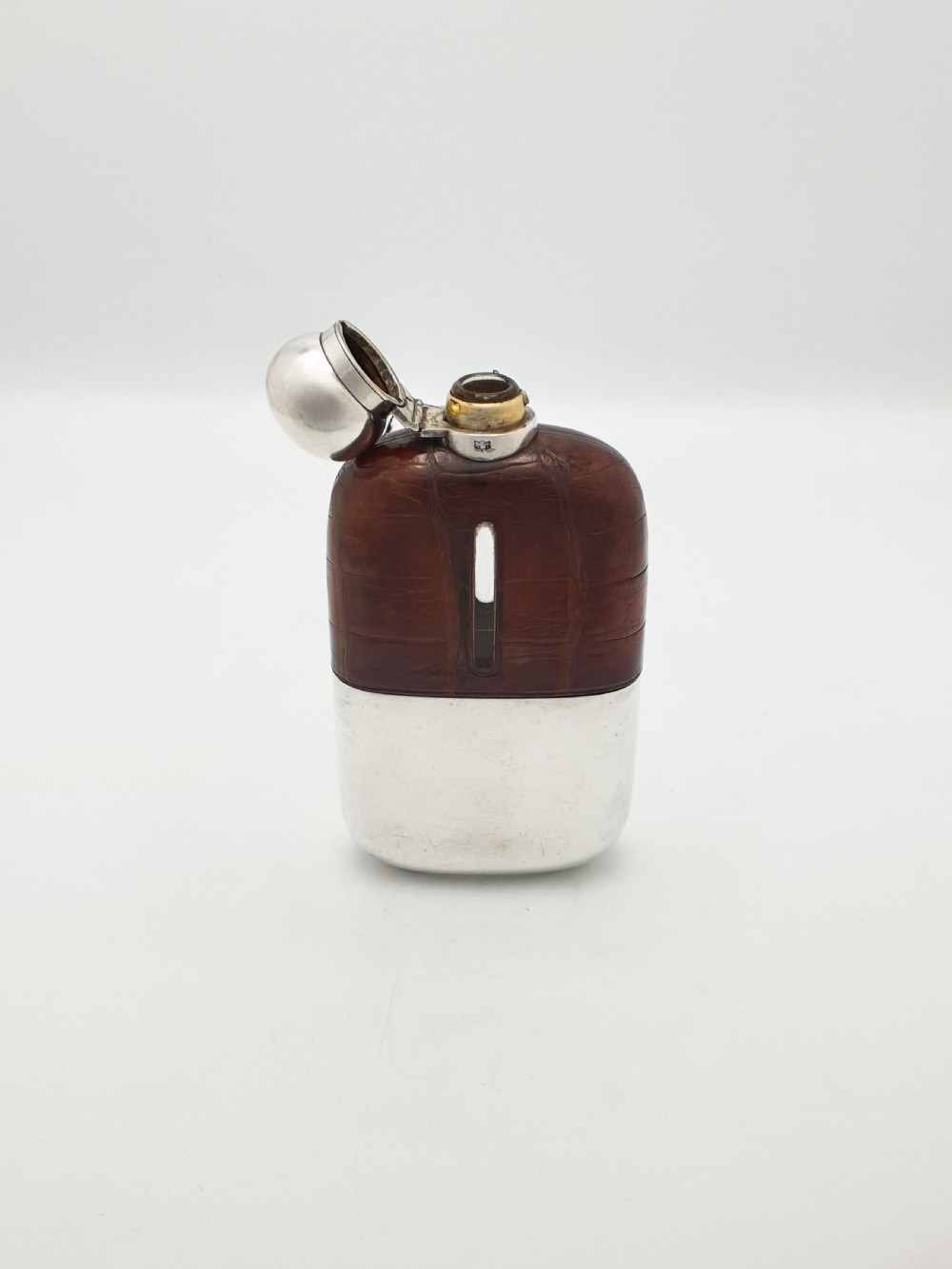 An antique Edwardian hip flask featuring a brown crocodile skin upper section with a vertical sight slot and a silver-plated lower removable cup. View III