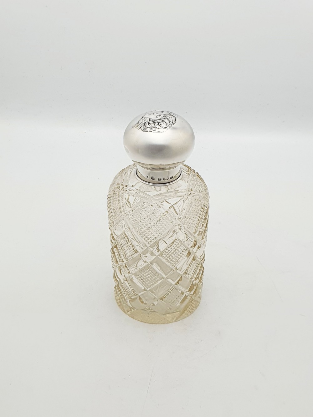An Edwardian clear cut glass scent bottle featuring a diamond faceted body and a sterling silver cap embossed with a cherub motif.