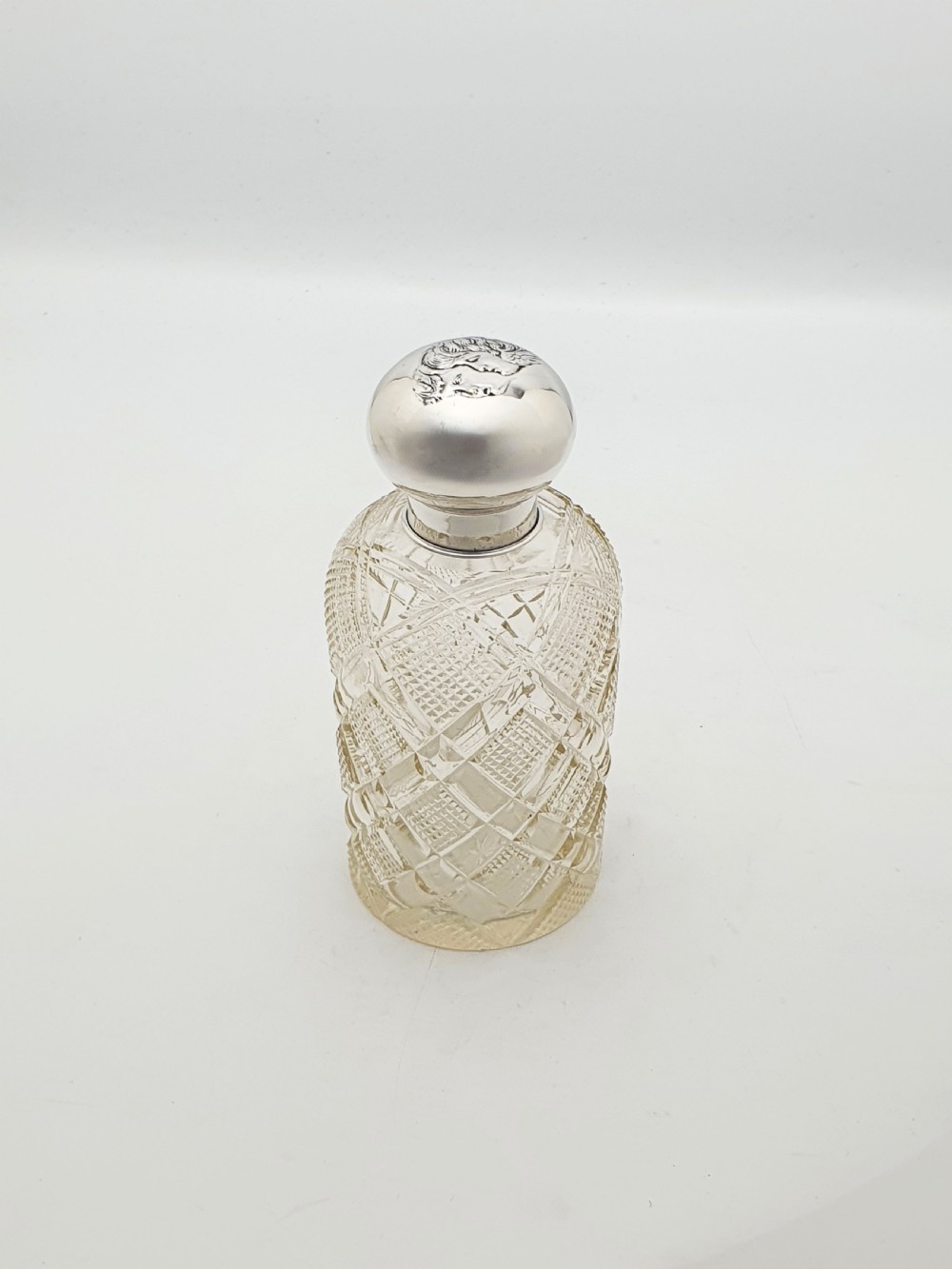 An Edwardian clear cut glass scent bottle featuring a diamond faceted body and a sterling silver cap embossed with a cherub motif. View II