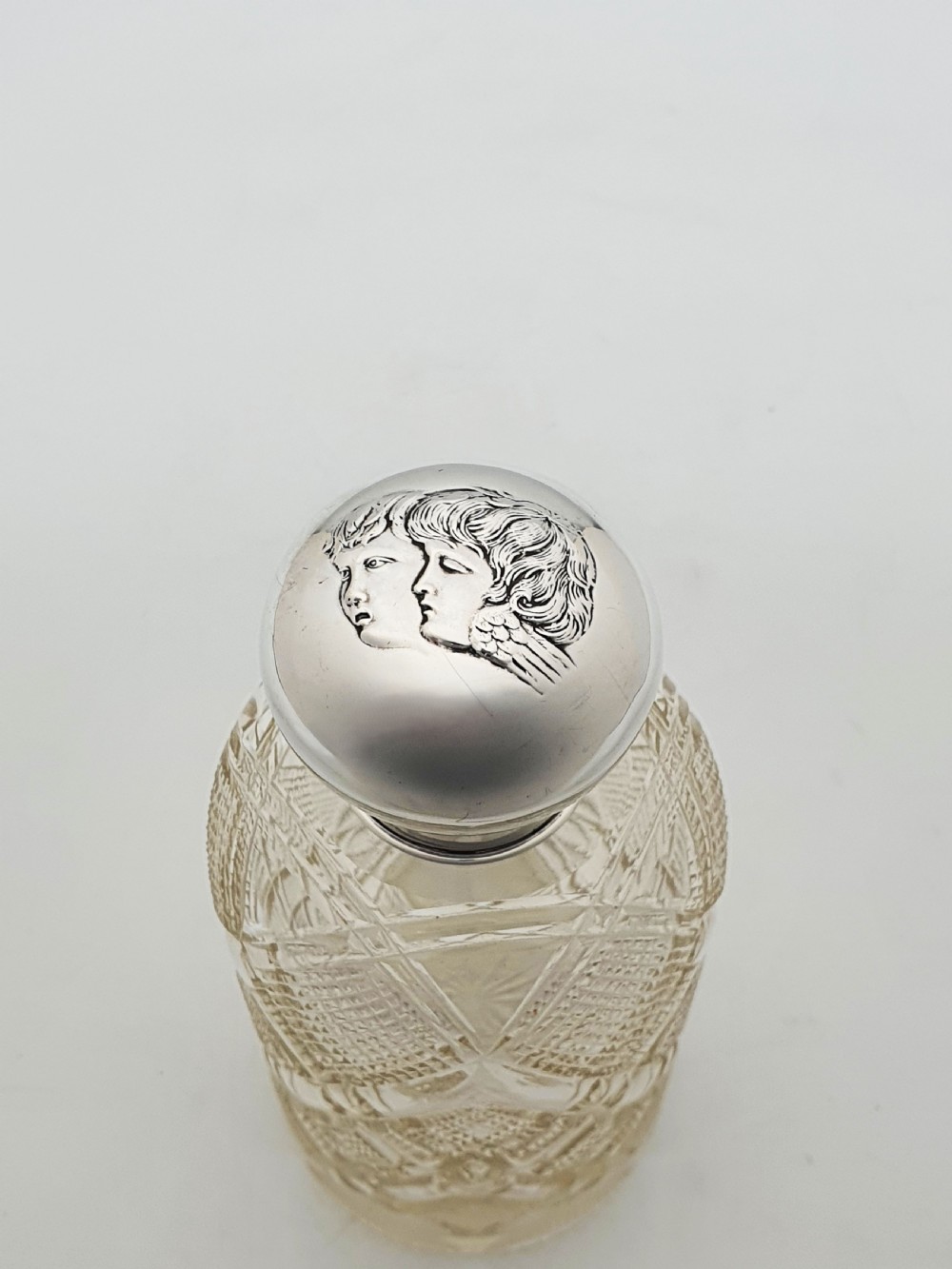 An Edwardian clear cut glass scent bottle featuring a diamond faceted body and a sterling silver cap embossed with a cherub motif. View IV