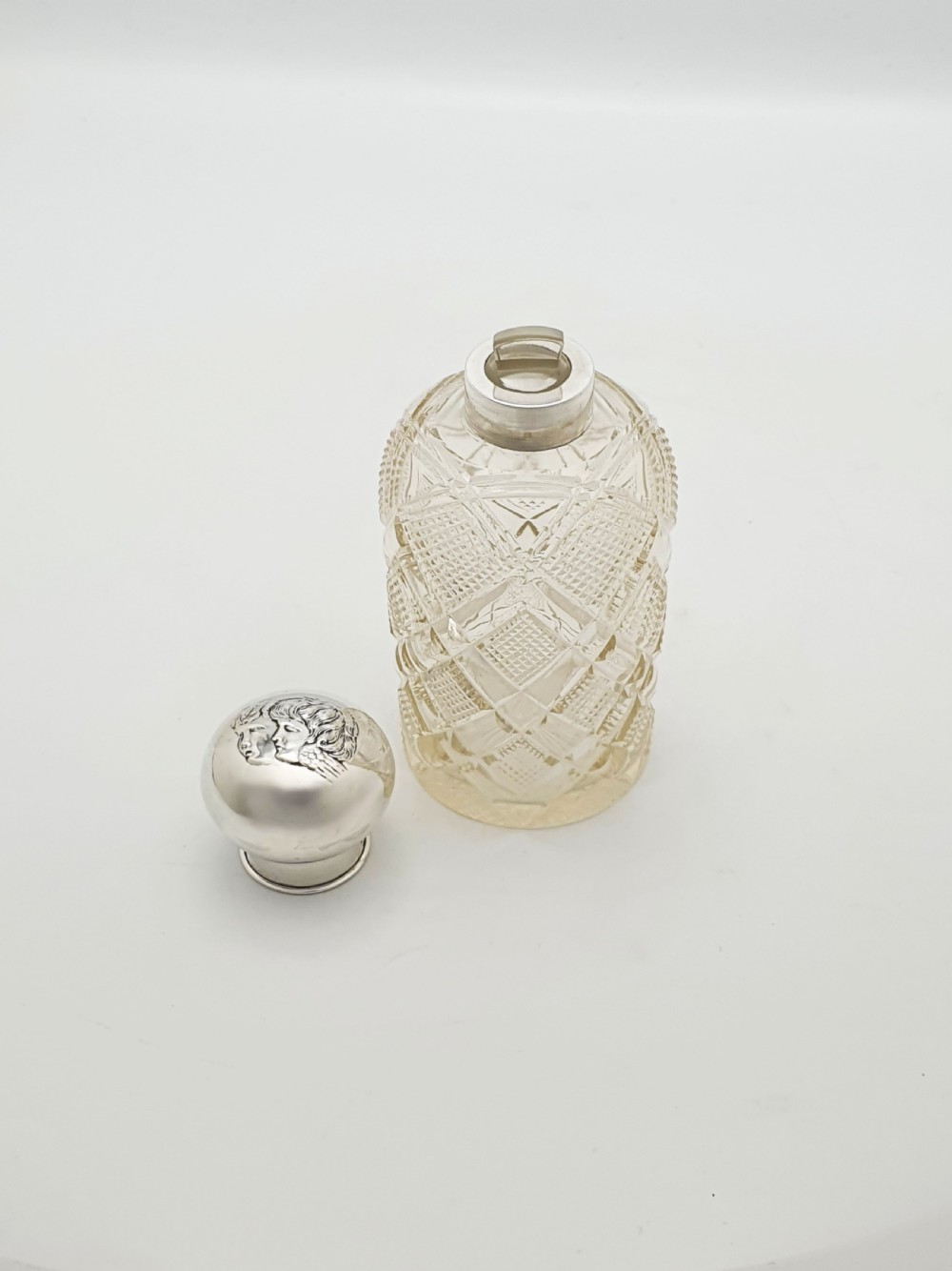 An Edwardian clear cut glass scent bottle featuring a diamond faceted body and a sterling silver cap embossed with a cherub motif. View V