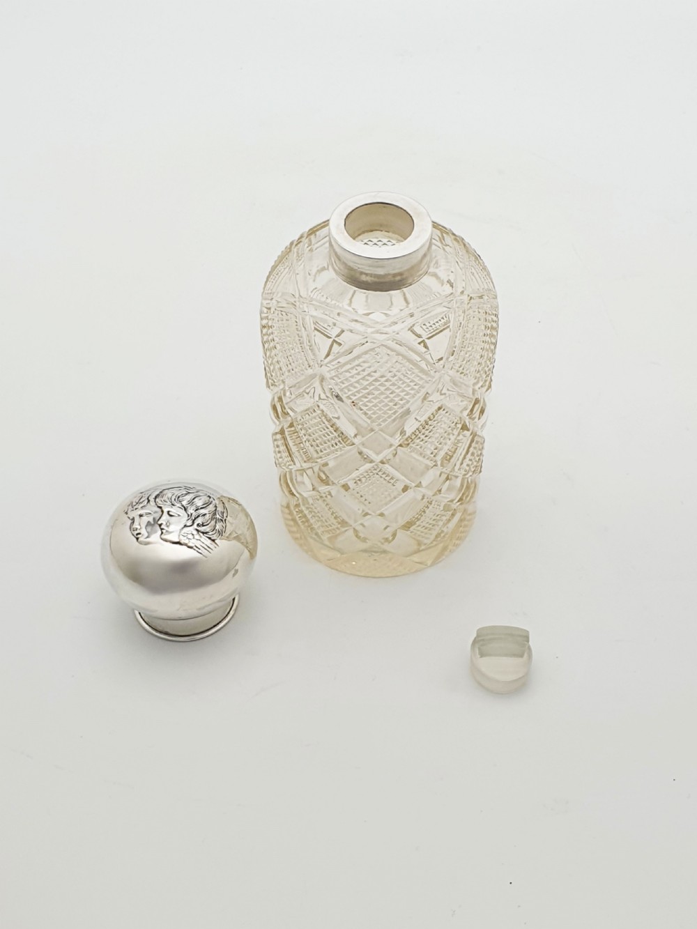 An Edwardian clear cut glass scent bottle featuring a diamond faceted body and a sterling silver cap embossed with a cherub motif. View VI