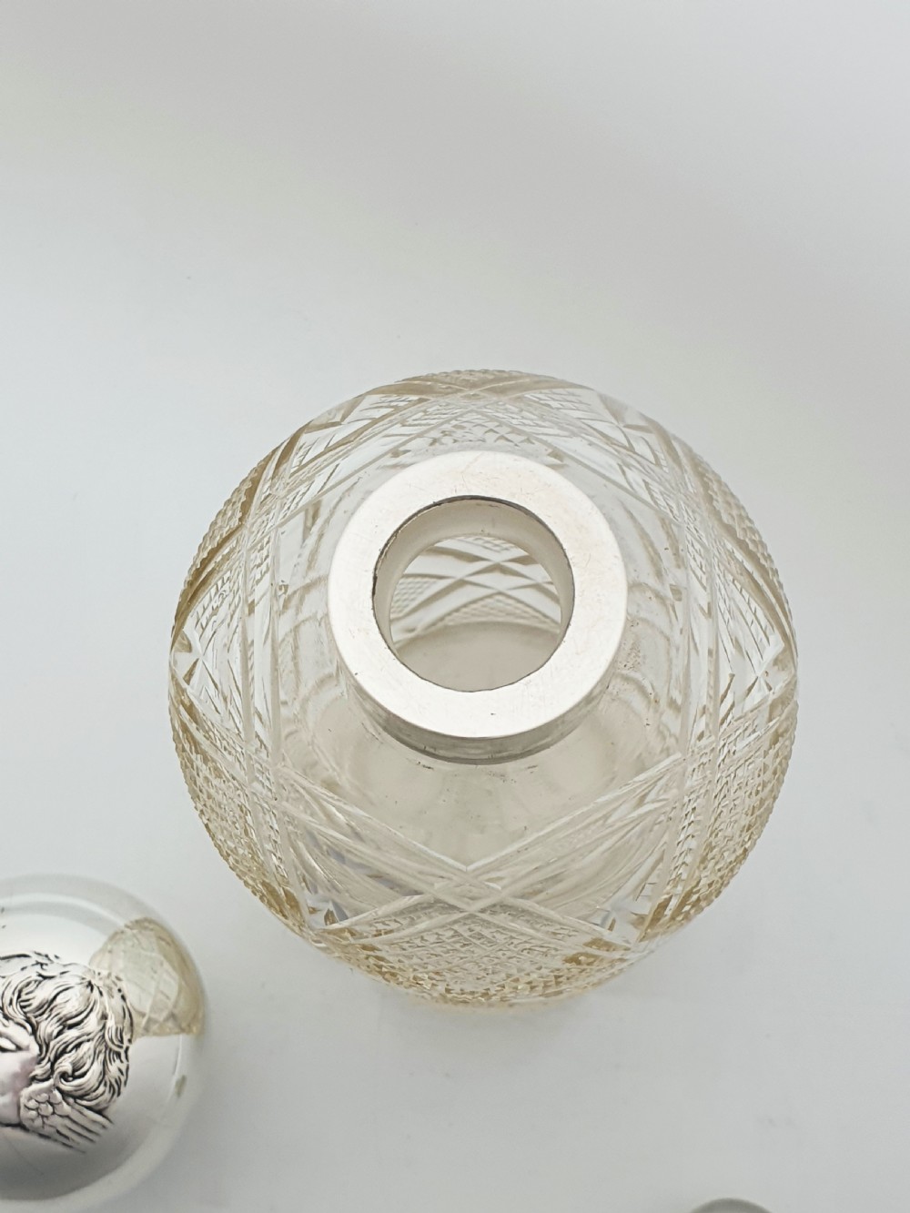 An Edwardian clear cut glass scent bottle featuring a diamond faceted body and a sterling silver cap embossed with a cherub motif. View VII