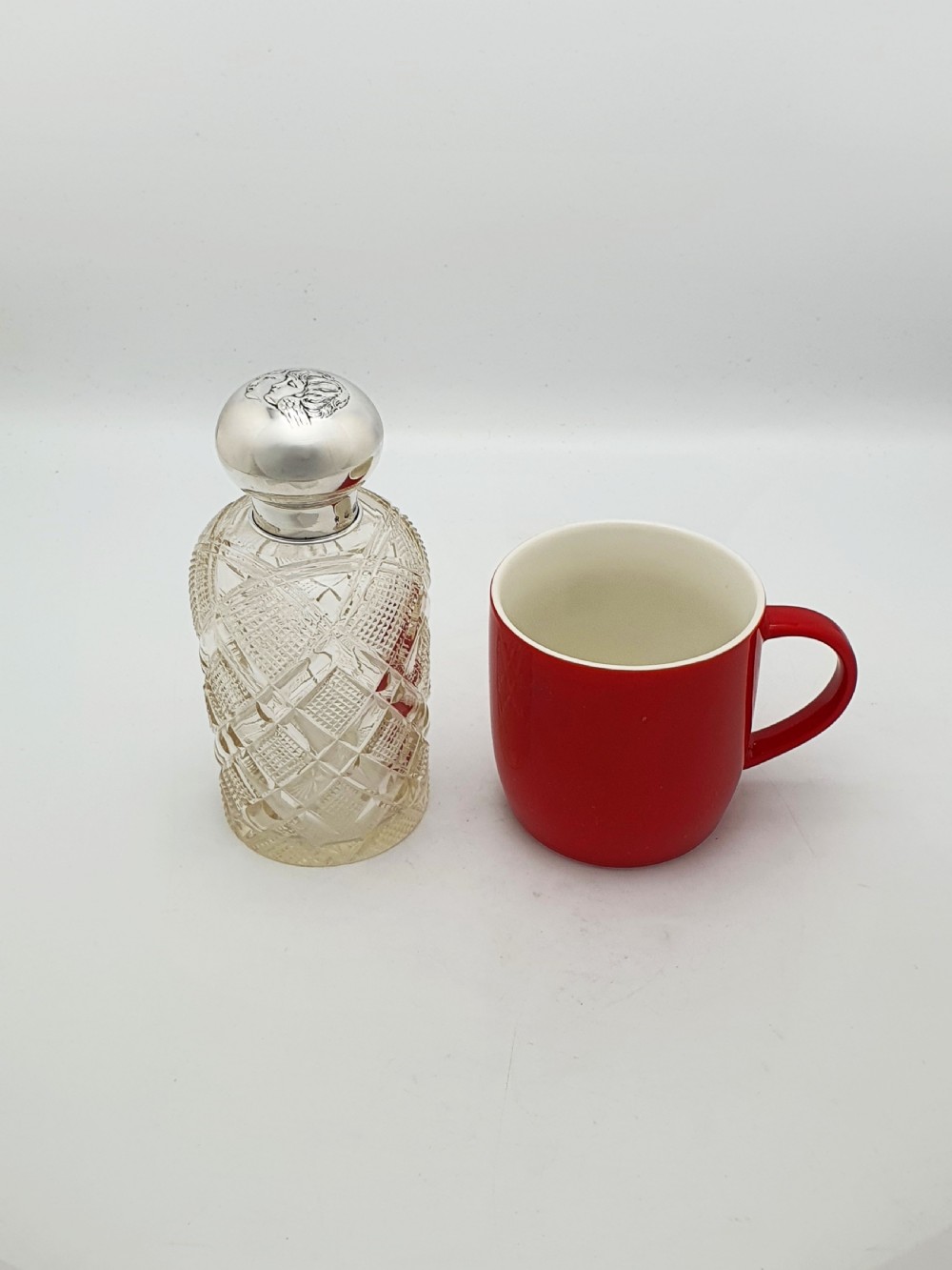 An Edwardian clear cut glass scent bottle featuring a diamond faceted body and a sterling silver cap embossed with a cherub motif. View IX