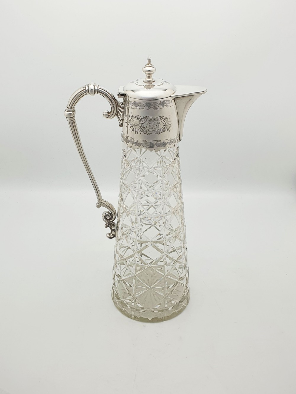 A tall Victorian cut glass claret jug featuring geometric diamond-cut motifs and an engraved silver-plated mount with a hinged lid and scrolled handle. View II