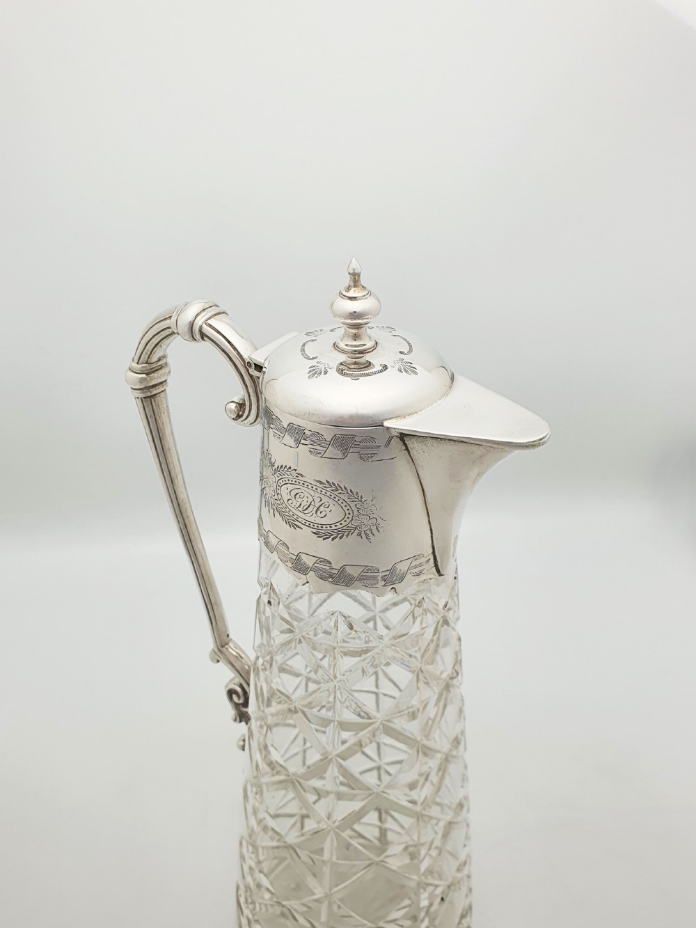 A tall Victorian cut glass claret jug featuring geometric diamond-cut motifs and an engraved silver-plated mount with a hinged lid and scrolled handle. View IV