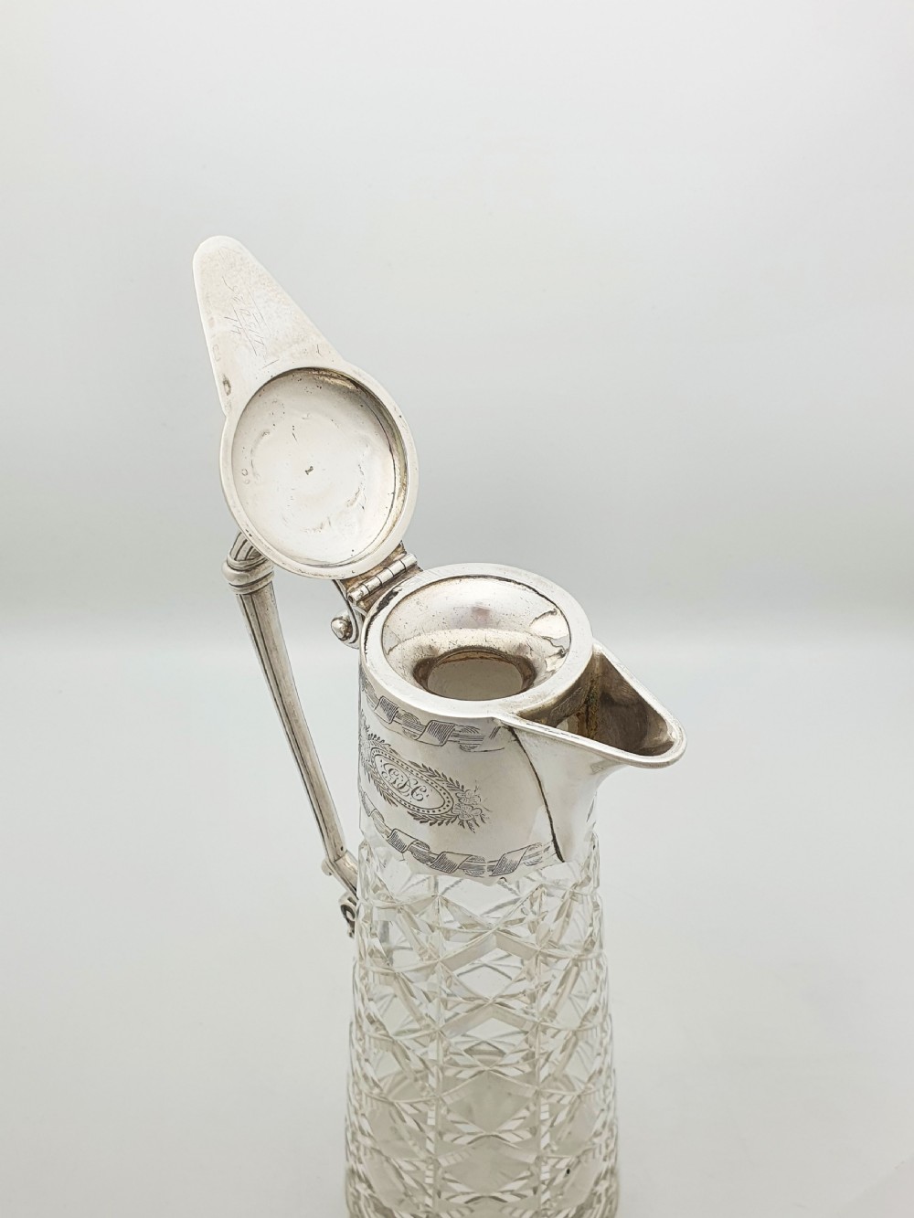 A tall Victorian cut glass claret jug featuring geometric diamond-cut motifs and an engraved silver-plated mount with a hinged lid and scrolled handle. View V