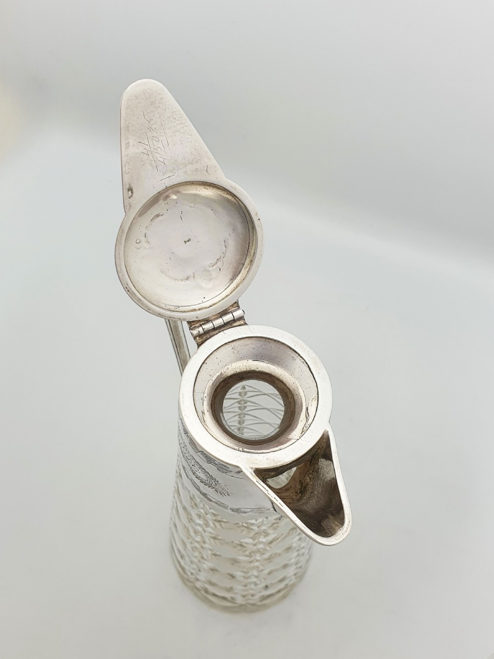 A tall Victorian cut glass claret jug featuring geometric diamond-cut motifs and an engraved silver-plated mount with a hinged lid and scrolled handle. View VI