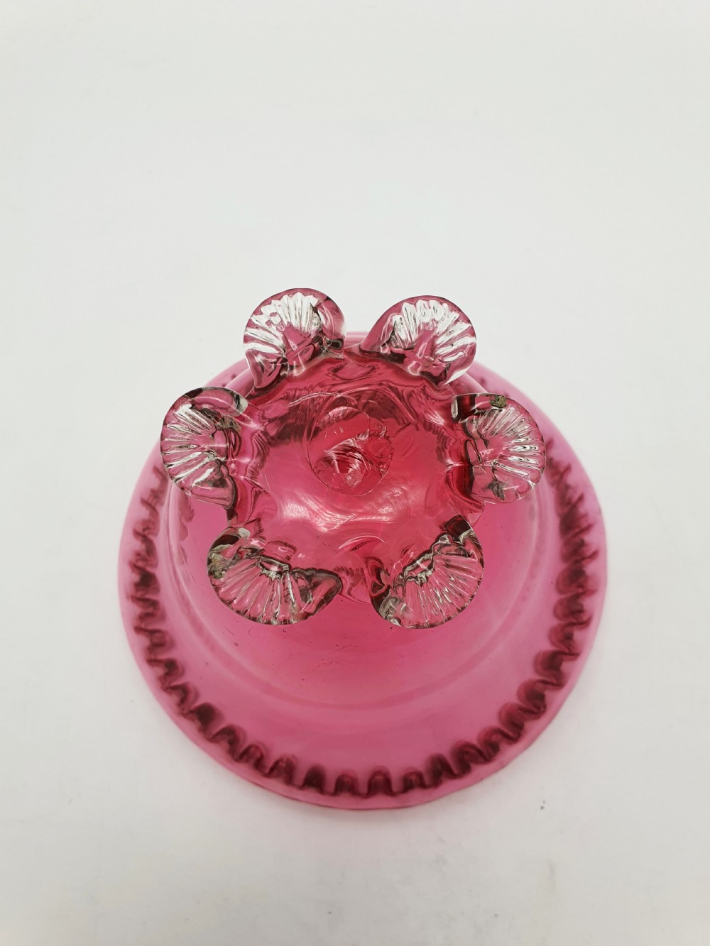A Victorian cranberry glass bowl with a crimped rim and applied feet, containing a metal pierced spoon. View V