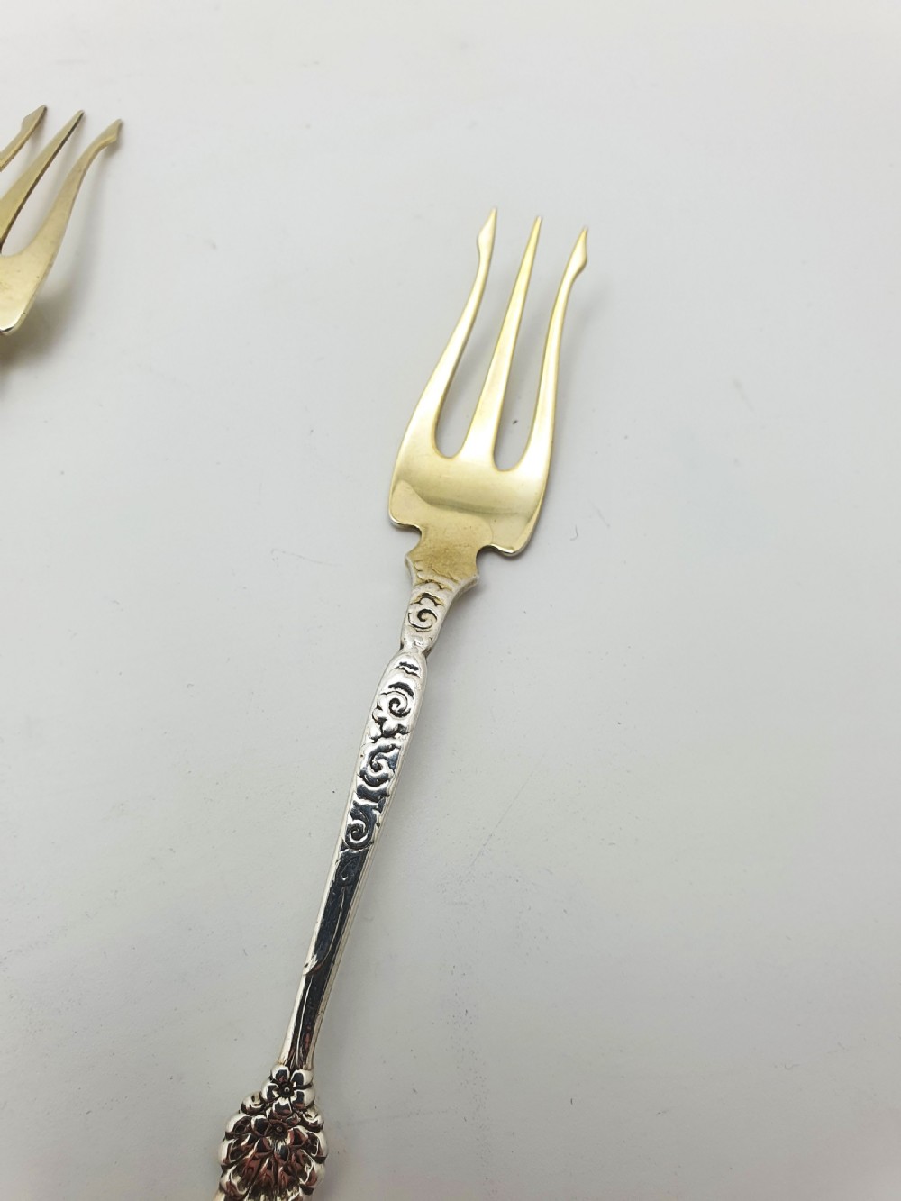 A set of twelve sterling silver seafood forks with ornate floral handles and gold gilt tines arranged in a diagonal line. View II