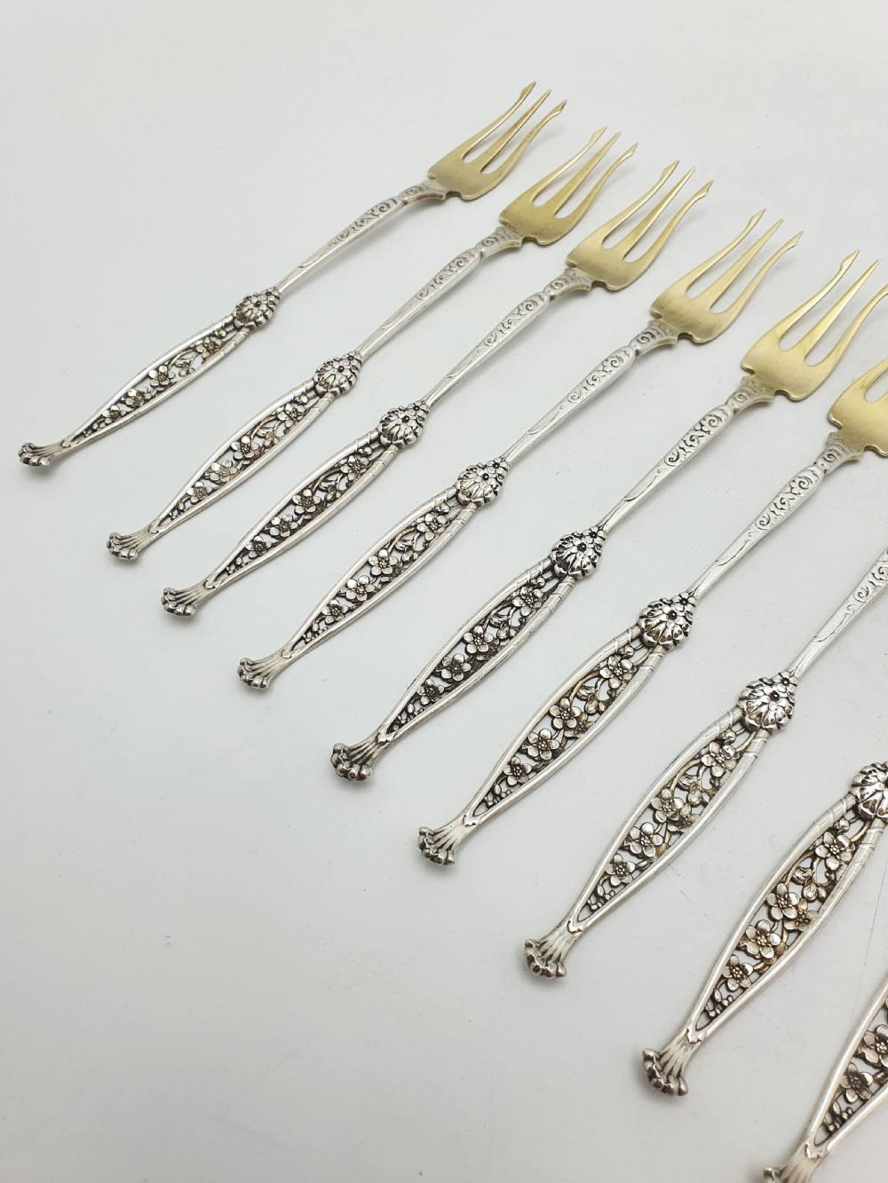 A set of twelve sterling silver seafood forks with ornate floral handles and gold gilt tines arranged in a diagonal line. View VI