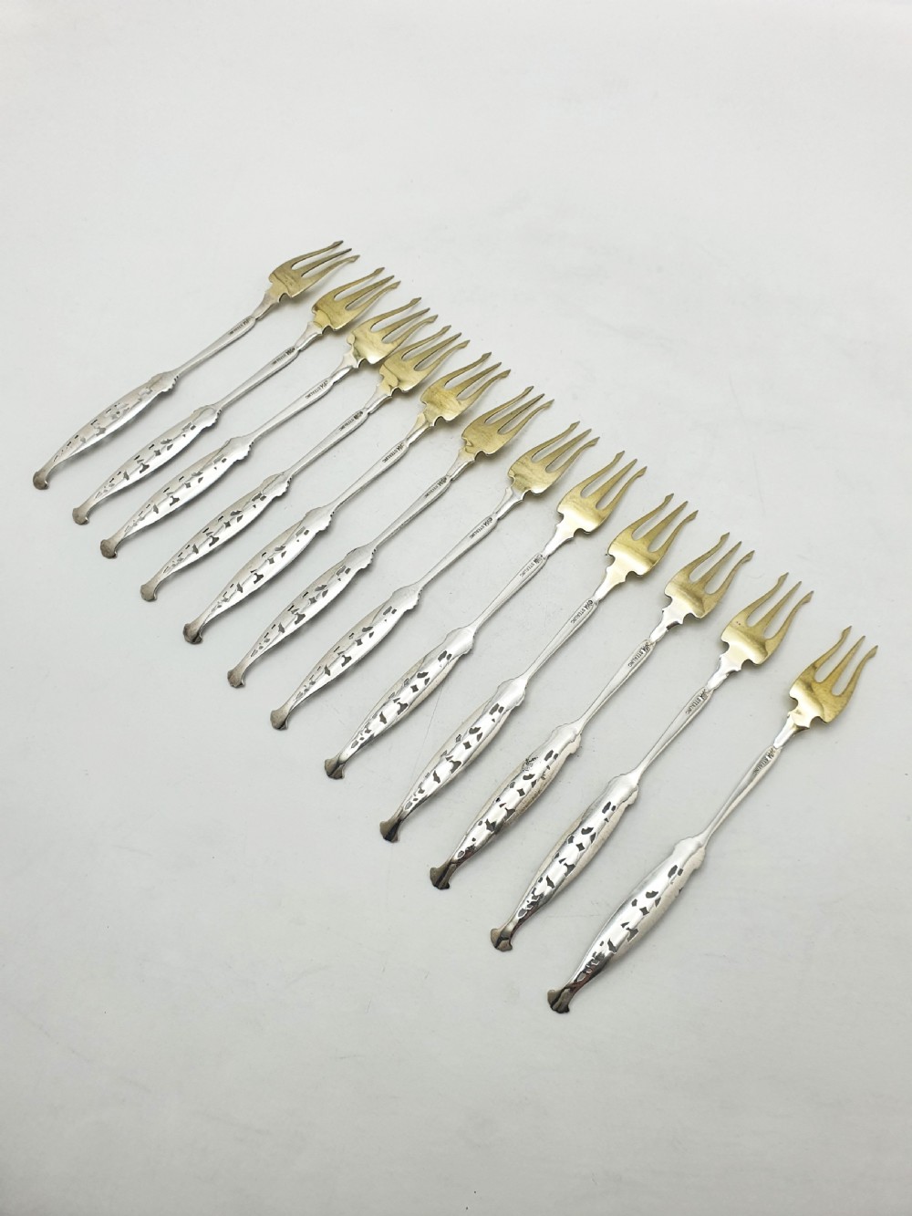 A set of twelve sterling silver seafood forks with ornate floral handles and gold gilt tines arranged in a diagonal line. View VIII