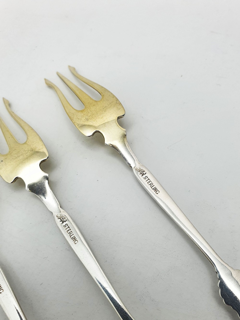 A set of twelve sterling silver seafood forks with ornate floral handles and gold gilt tines arranged in a diagonal line. View IX