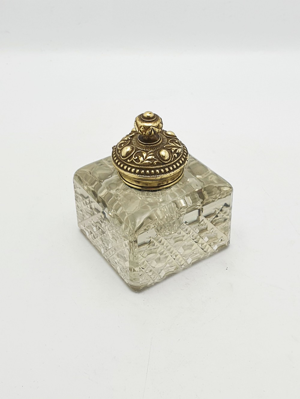 A square, heavy cut-glass antique inkwell featuring a diamond pattern and an ornate, embossed brass hinged lid.