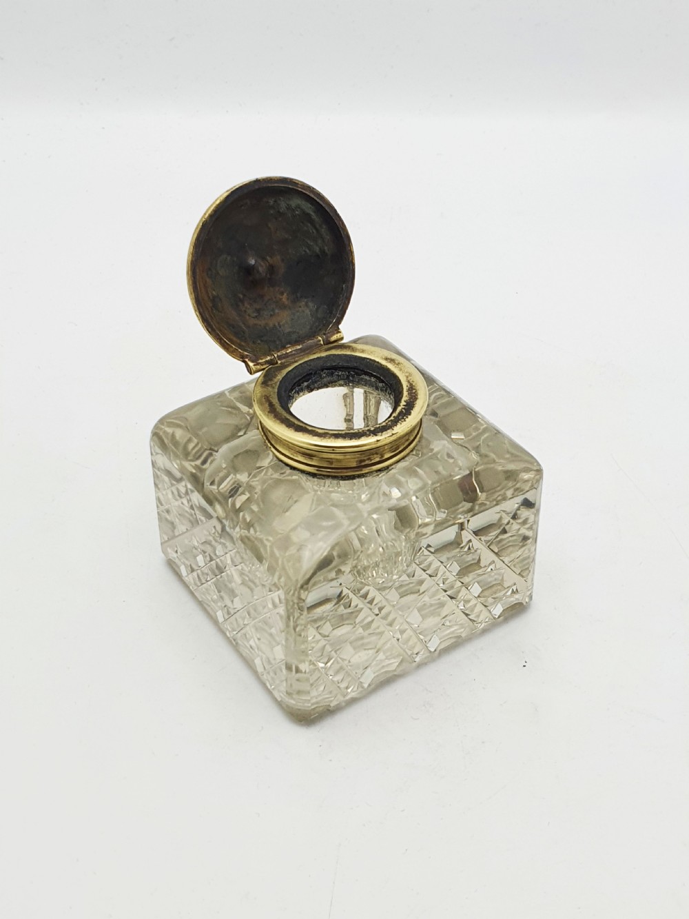 A square, heavy cut-glass antique inkwell featuring a diamond pattern and an ornate, embossed brass hinged lid. View II