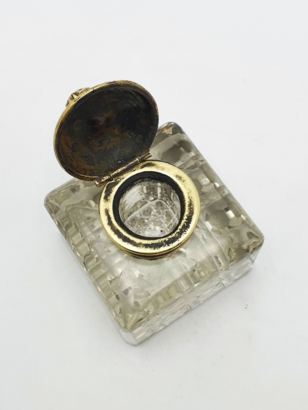 A square, heavy cut-glass antique inkwell featuring a diamond pattern and an ornate, embossed brass hinged lid. View III