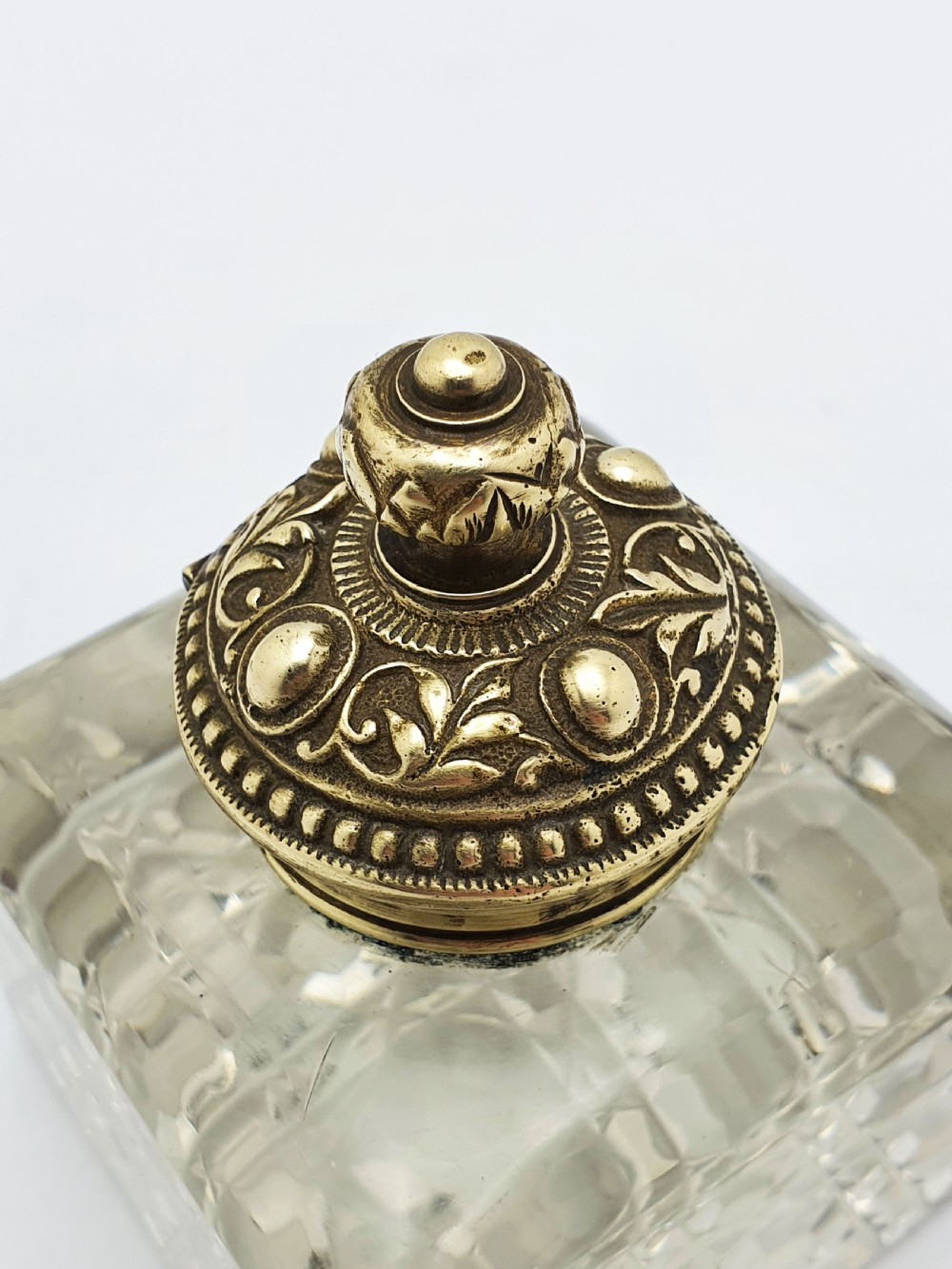 A square, heavy cut-glass antique inkwell featuring a diamond pattern and an ornate, embossed brass hinged lid. View IV