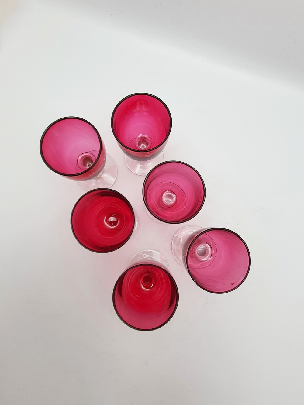 A set of six Victorian hand-blown wine glasses featuring deep cranberry red rounded bowls atop clear glass stems and circular bases. View IV