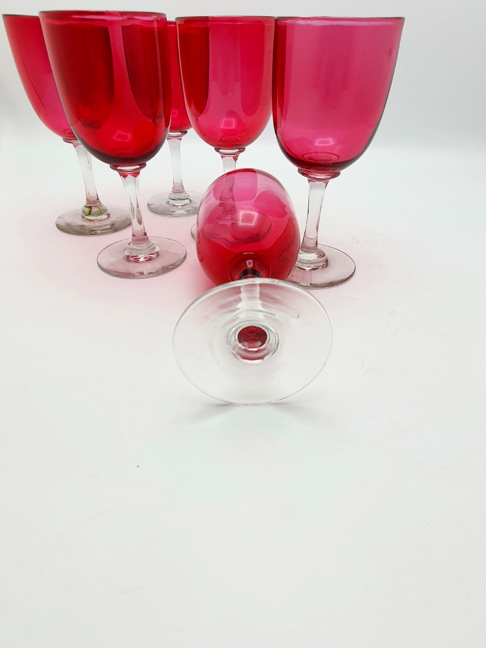 A set of six Victorian hand-blown wine glasses featuring deep cranberry red rounded bowls atop clear glass stems and circular bases. View V